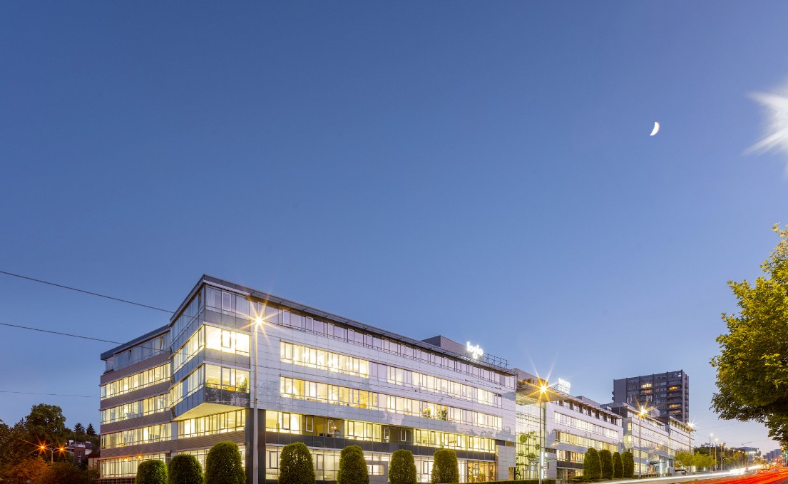 Modern office building at twilight with illuminated windows, a clear blue sky, and a crescent moon. [AI-generated text]