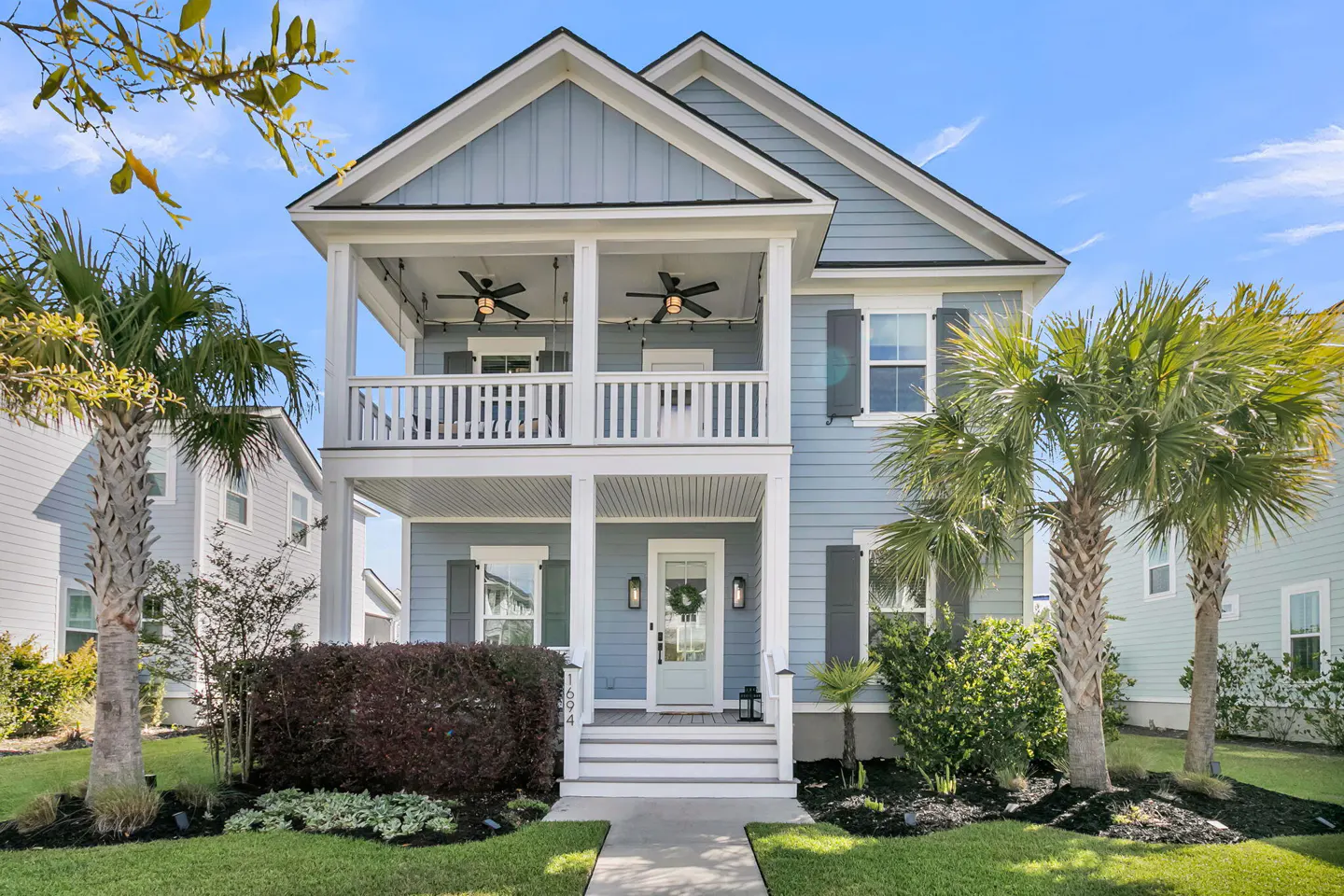 Two-story light blue house with white trim, a double porch, and palm trees in the front yard.