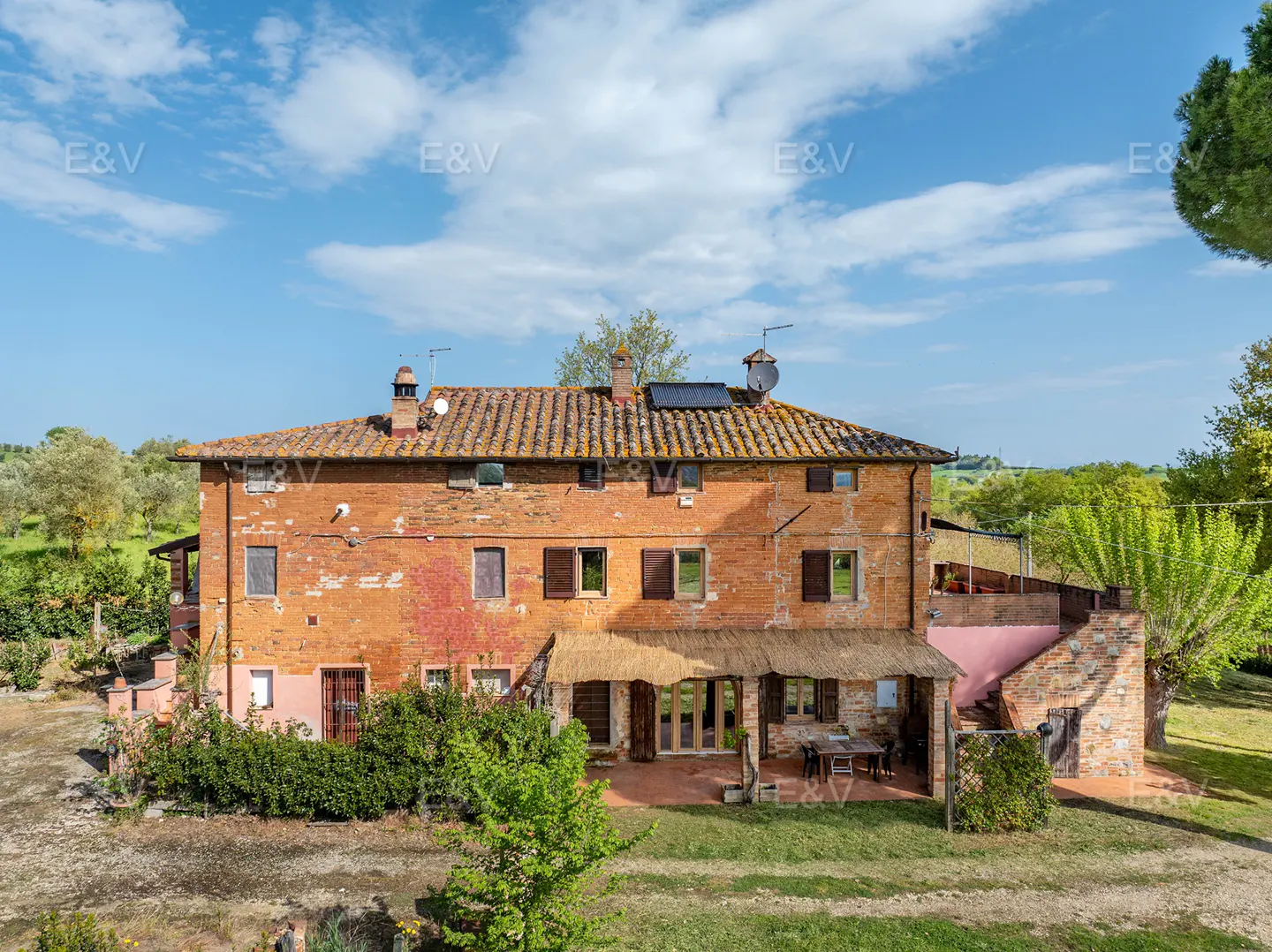 Exterior of a two-story brick farmhouse with a tile roof, a covered patio, and green grass.