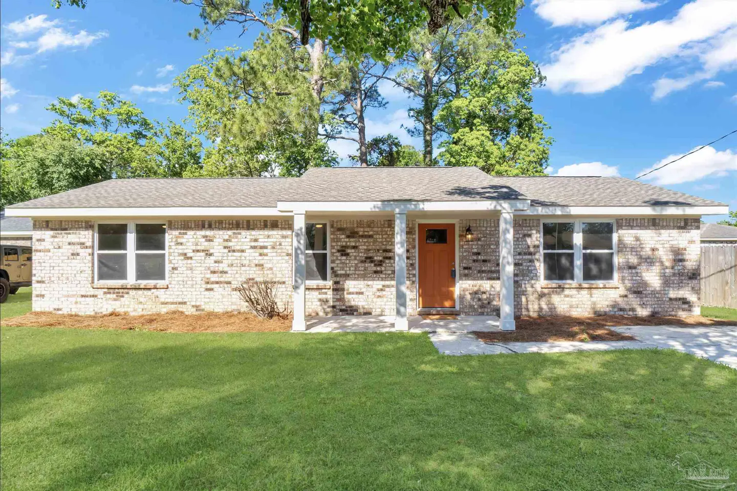 A single-story brick house with an orange front door and a green lawn under a blue sky.