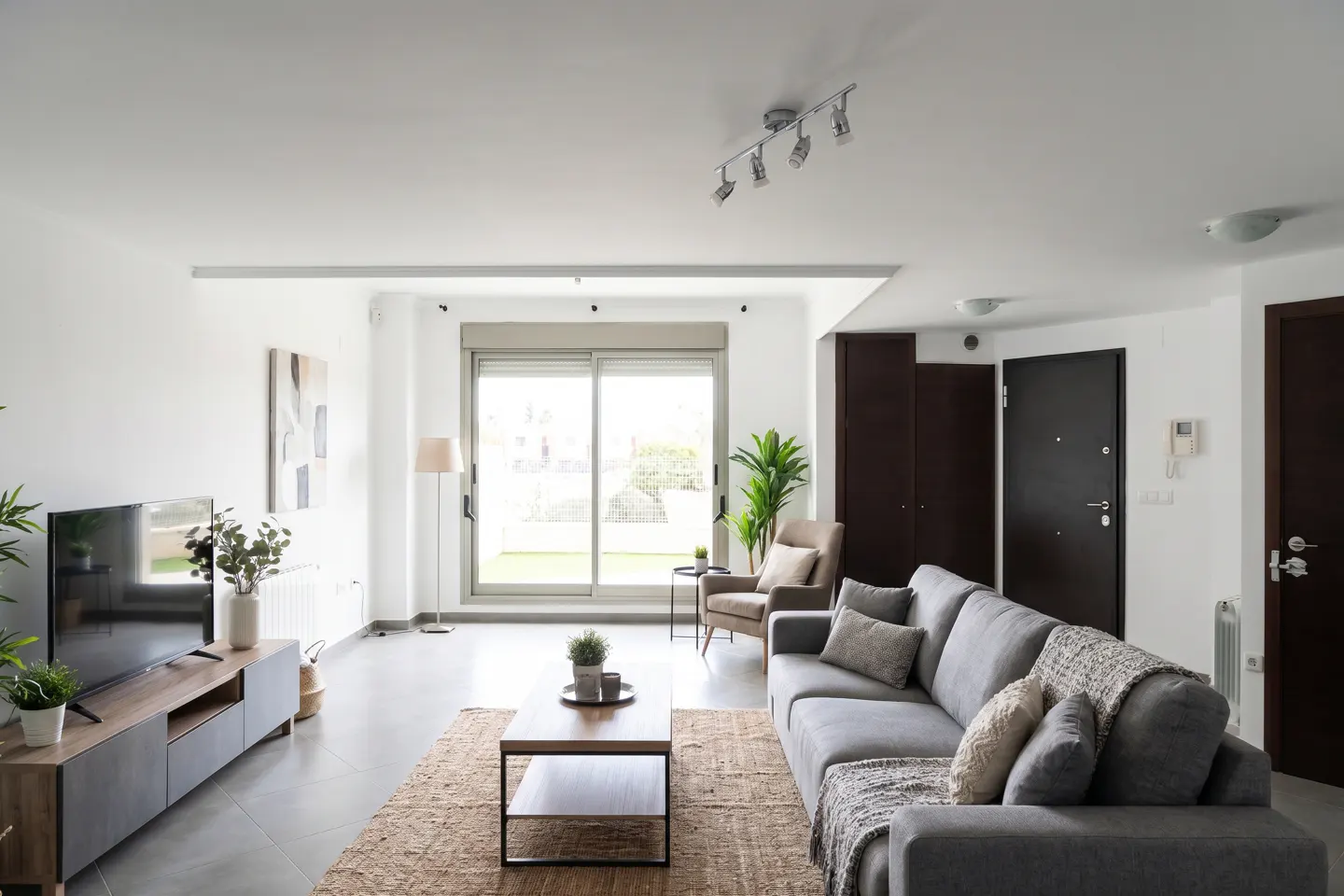Bright living room with a gray sofa, wood coffee table on a jute rug, and a large window with a view of greenery.