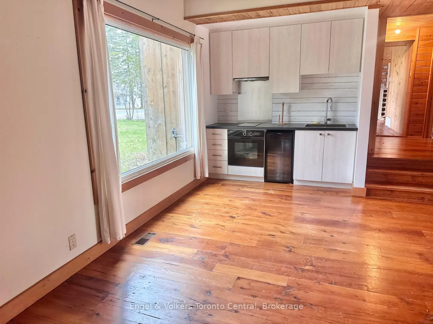A bright kitchen with wood floors, white cabinets, and a large window with a view of a green lawn.
