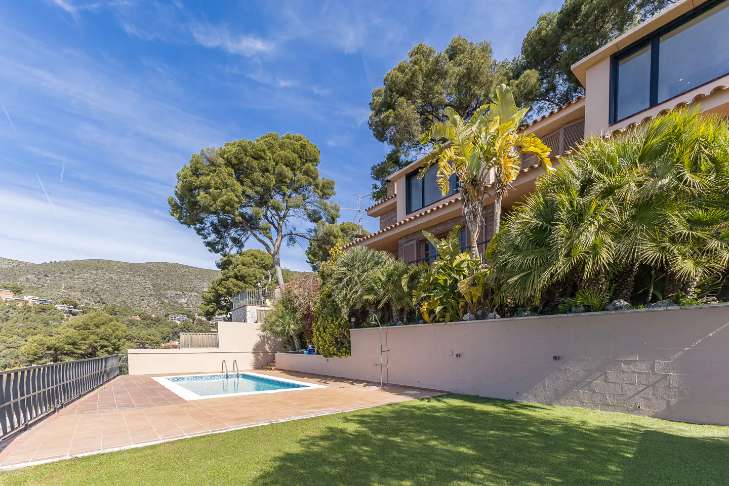Luxury home exterior with a pool, green lawn, and lush tropical landscaping on a sunny day.