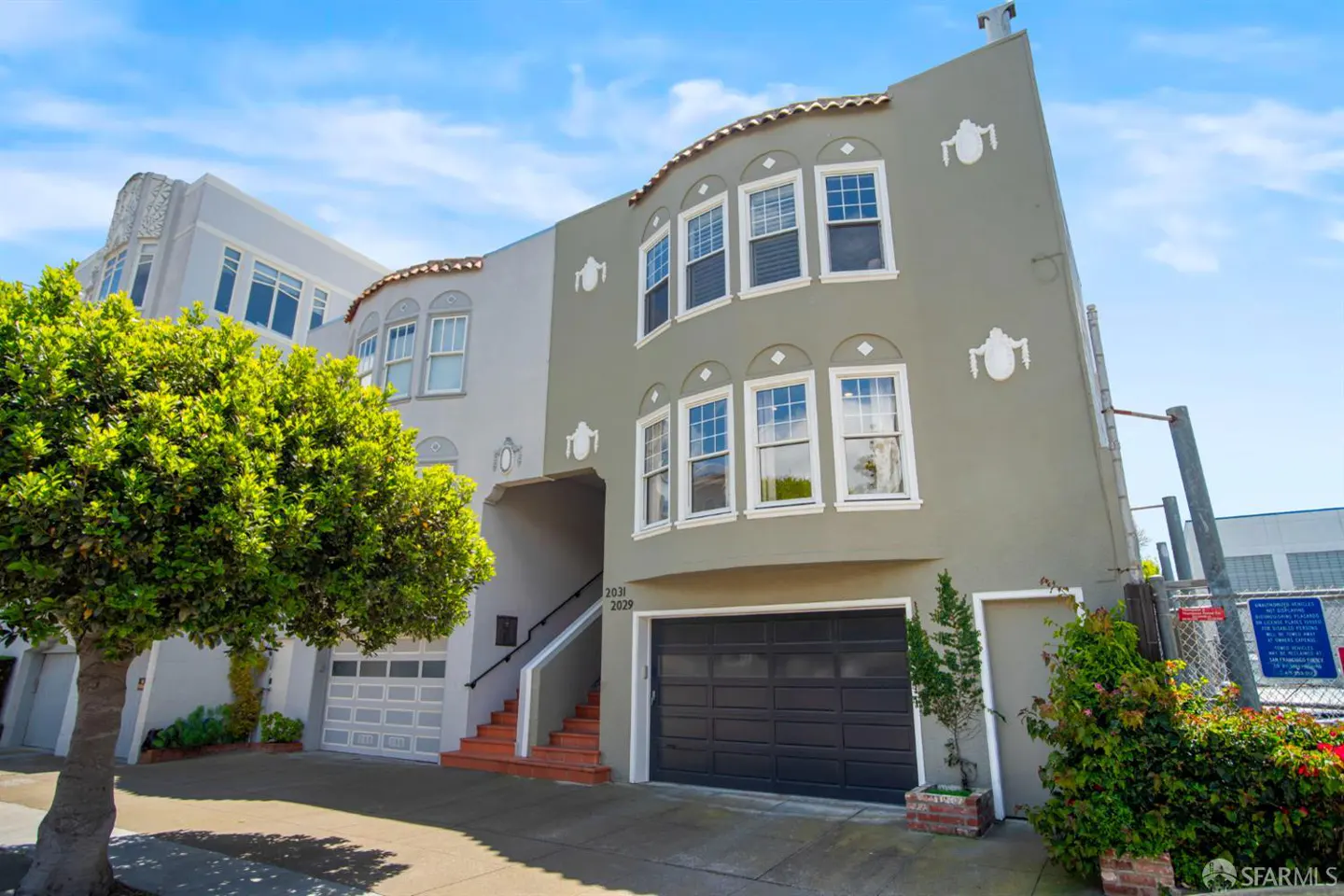 Exterior view of a two-story, gray row house with a black garage door and bay windows under a blue sky.