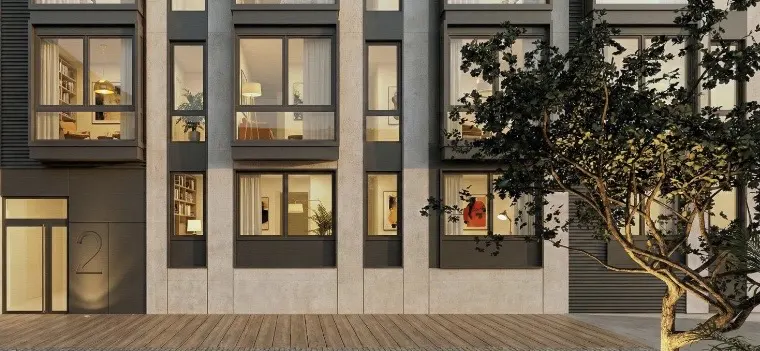 Modern apartment building exterior with large windows, gray trim, and a wooden walkway. A tree is on the right side.