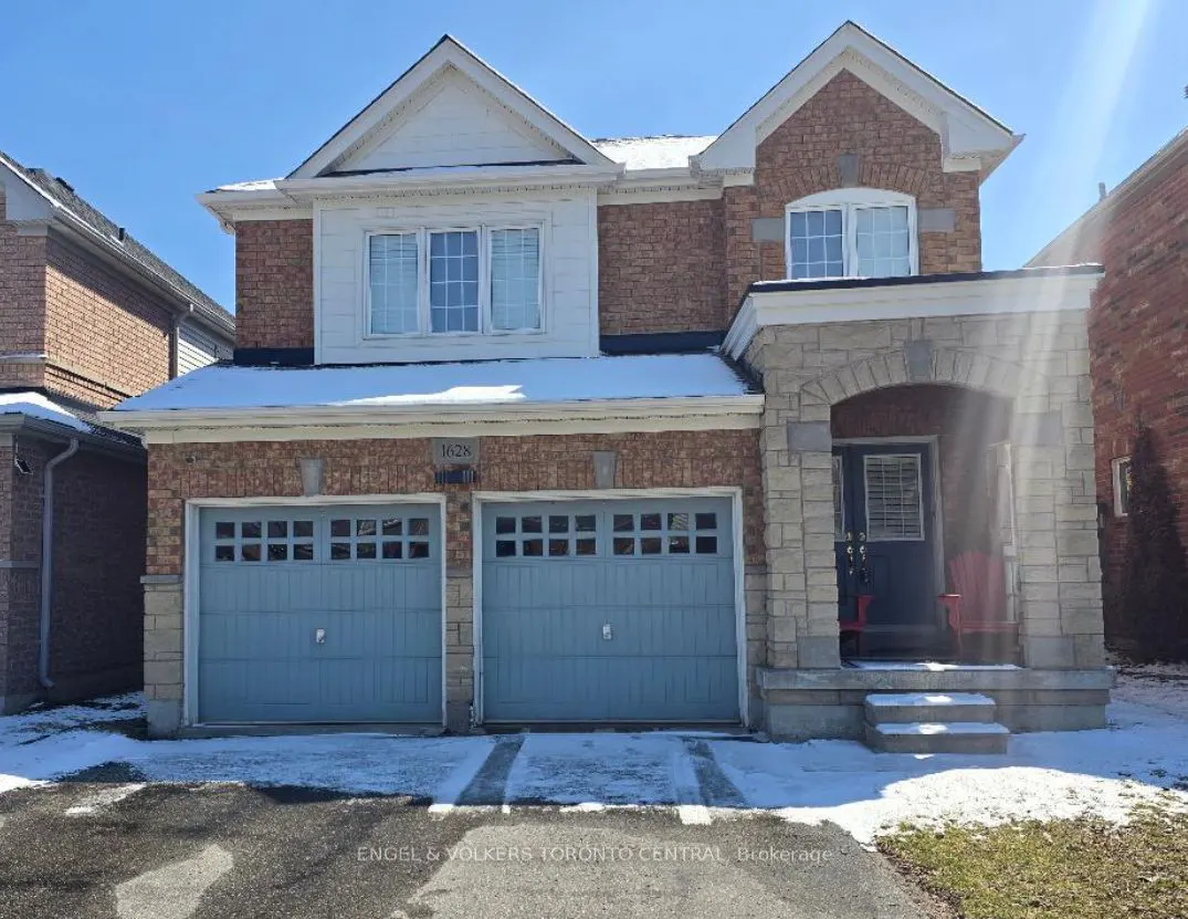 Two-story brick house with blue garage doors and stone porch. Snow on the roof and ground. Blue sky.