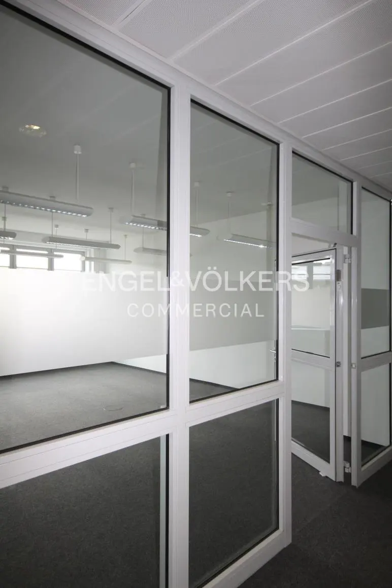 View of a commercial space with white walls, gray carpet, and glass windows. The Engel & Völkers logo is visible on the glass.