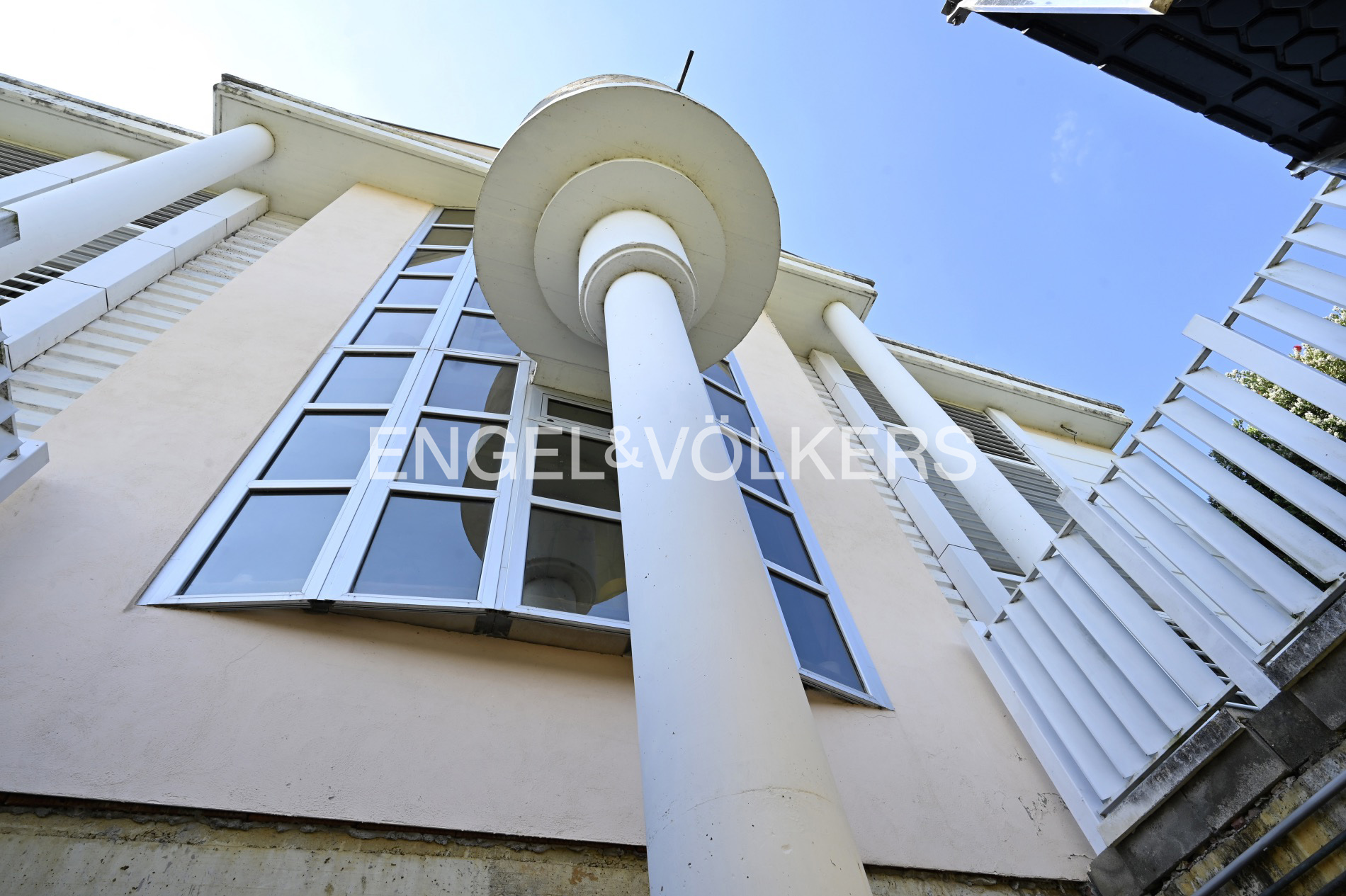 Low angle view of a building with large windows, white columns, and a blue sky.