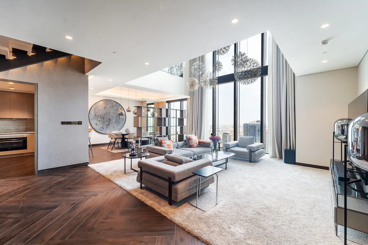 Bright, modern living room with gray sofas, a large window with city views, and a herringbone wood floor.
