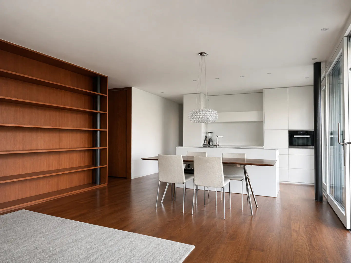 Bright, modern kitchen and dining area with wood floors, white cabinets, and a large wood bookshelf.