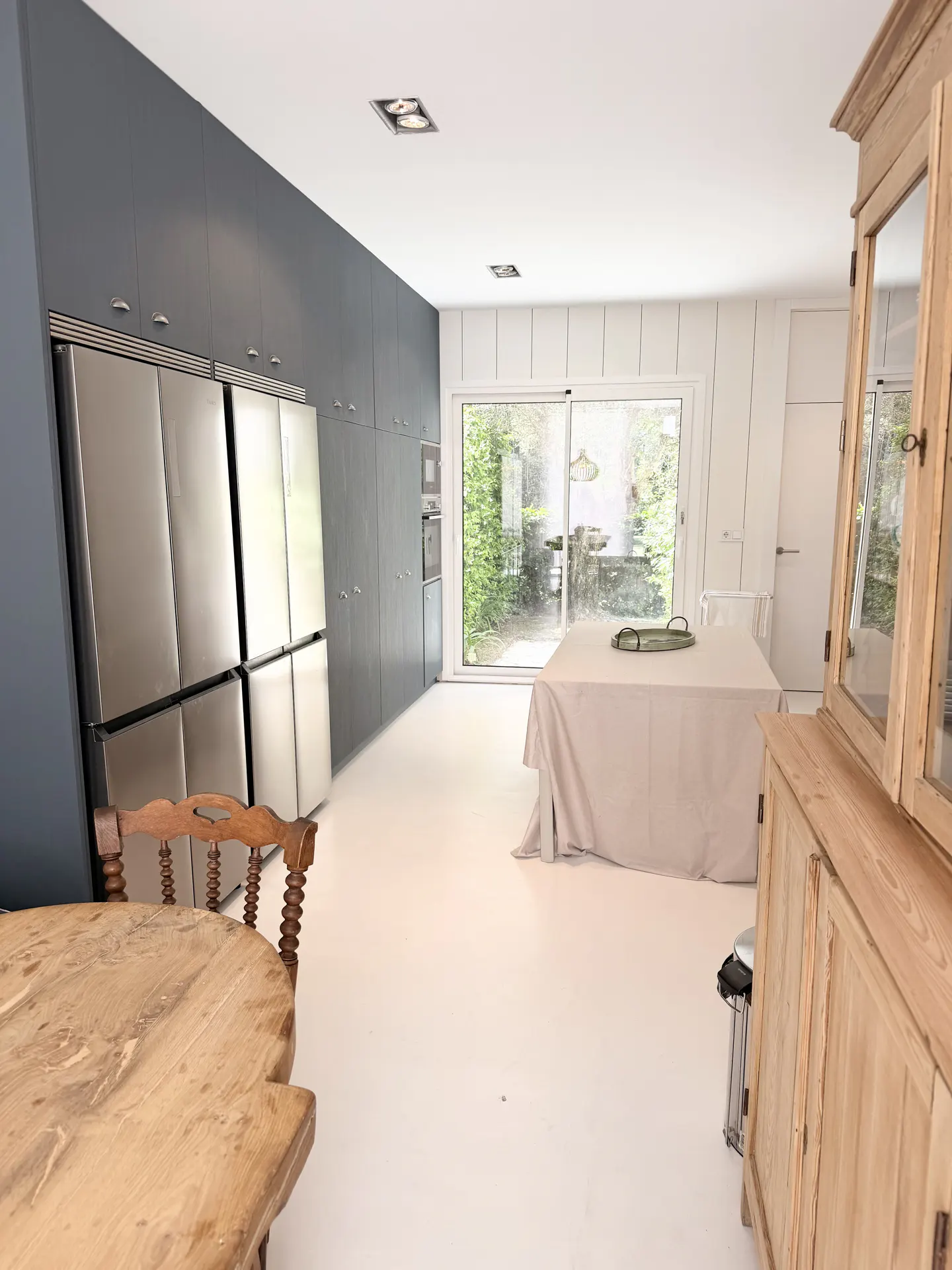 Bright kitchen with white floors, gray cabinets, and stainless steel appliances. A table with a white tablecloth sits near sliding glass doors.