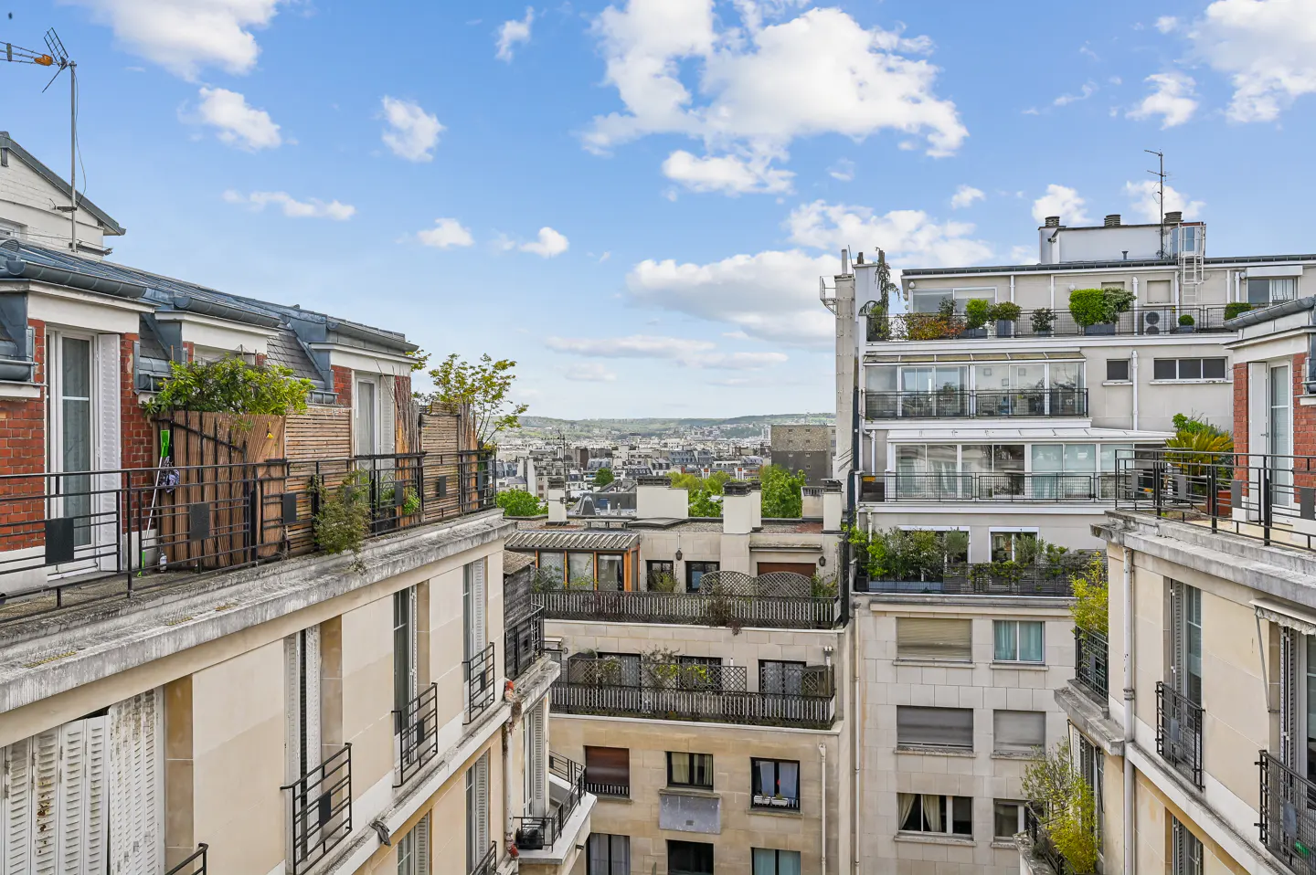 View of Parisian rooftops with balconies and greenery under a blue sky with scattered clouds.