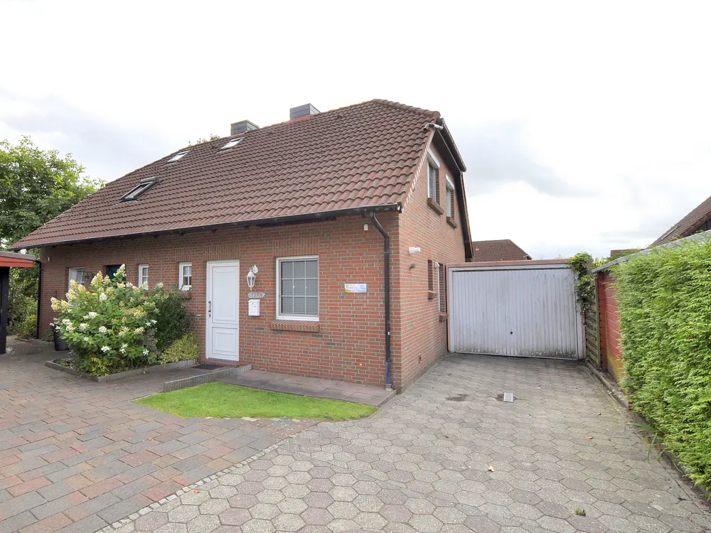 A red brick house with a brown tiled roof, white front door, attached garage, and a paved driveway.