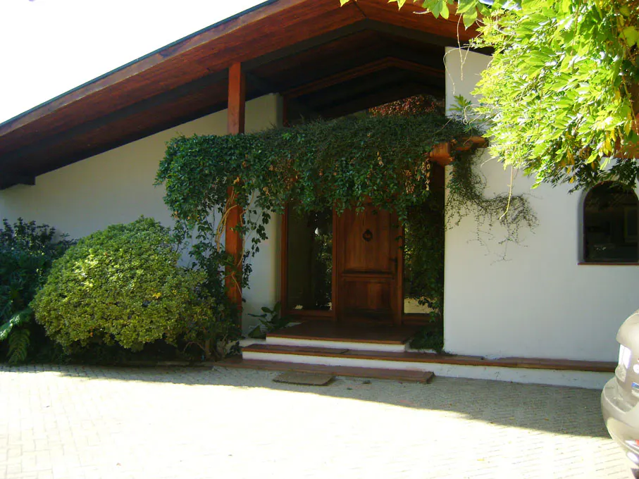 Front view of a house with a brown wooden door and a white wall covered with green plants.