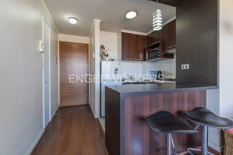 A kitchen with dark wood cabinets, a breakfast bar with two black stools, and a white refrigerator.