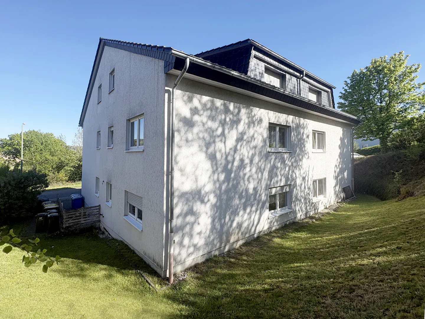 Exterior view of a three-story white building with a dark roof, surrounded by green grass and trees.