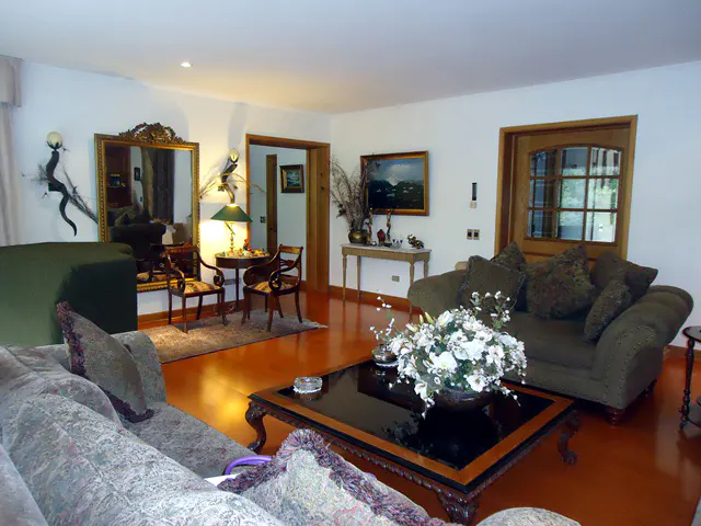 A living room with sofas, chairs, a coffee table, and a large mirror. The walls are white, and the floor is orange.