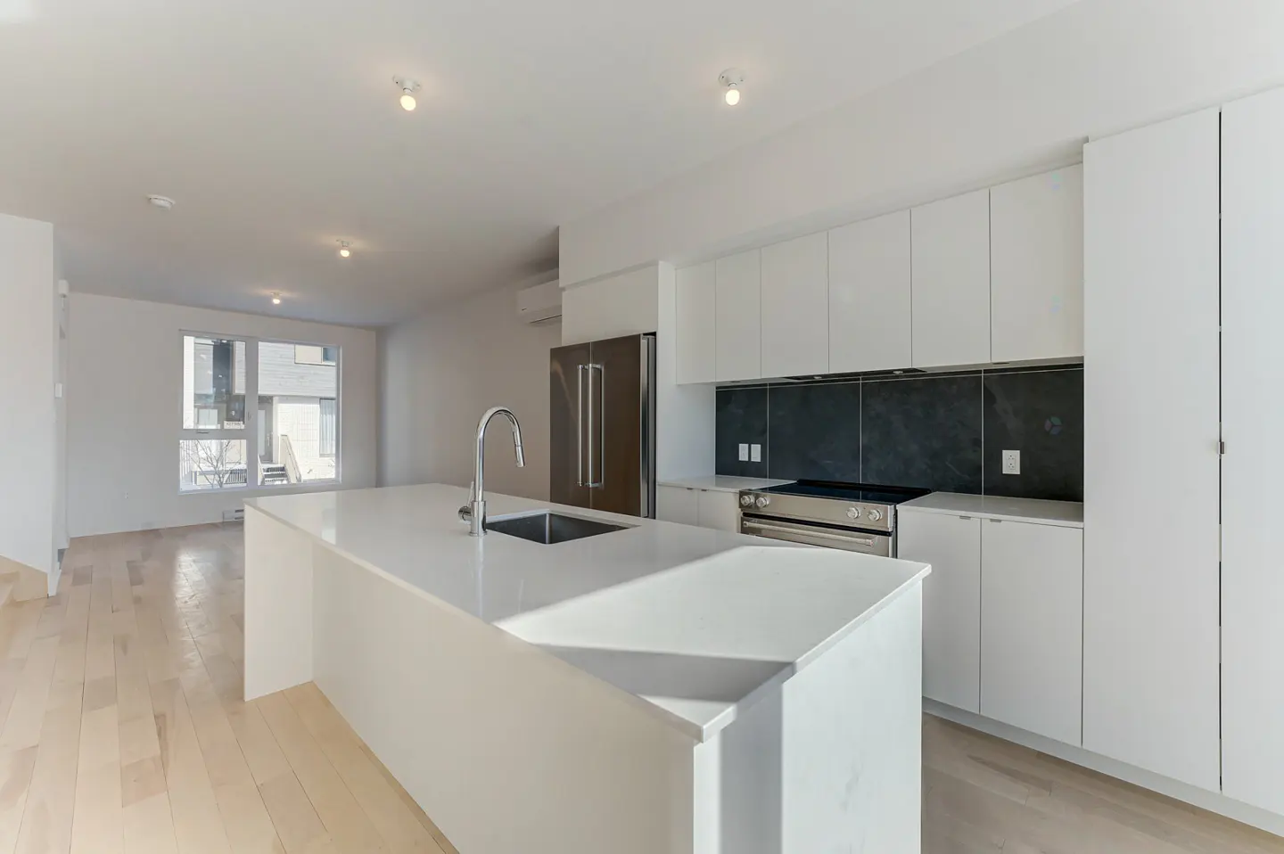 Bright, modern kitchen with white cabinets, stainless steel appliances, and a large island with a sink. Hardwood floors and natural light.