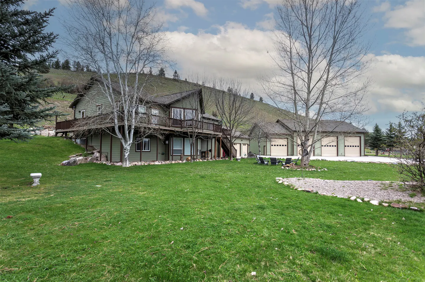 Two-story green house with a dark roof, a deck, and a three-car garage on a large green lawn.