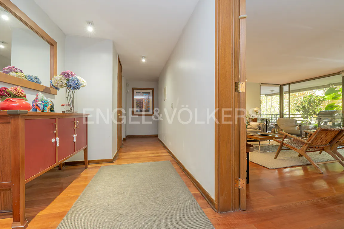 Hallway with wood floors, a red cabinet with flowers, and a view into a living room with floor-to-ceiling windows.