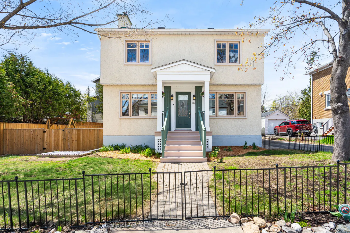 Two-story beige house with a green door and trim, a small front yard, and a black metal fence.