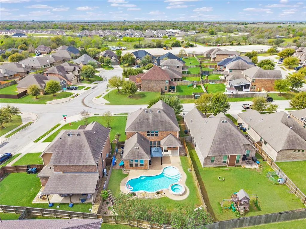 Aerial view of a suburban neighborhood with houses, green lawns, and a blue swimming pool in one backyard.