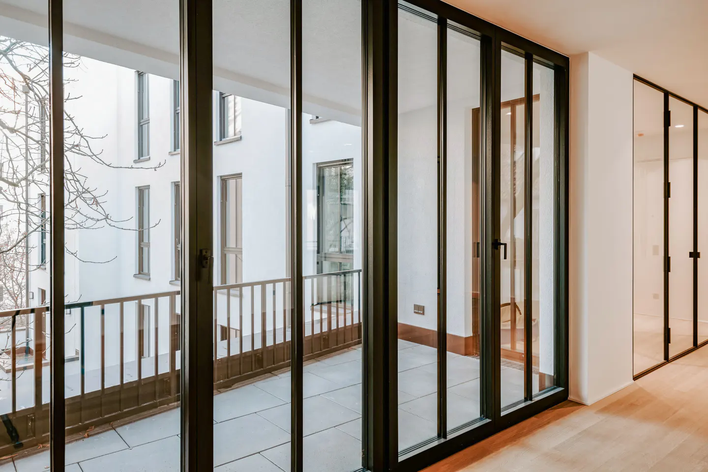 Interior view of a room with black-framed glass doors leading to a balcony with a white building in the background.