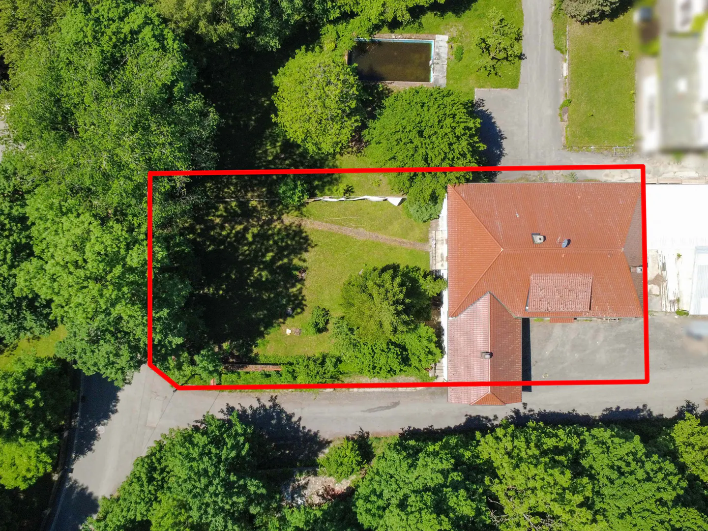 Aerial view of a house with a red-tiled roof and a large, tree-lined backyard outlined in red, including a small pool.