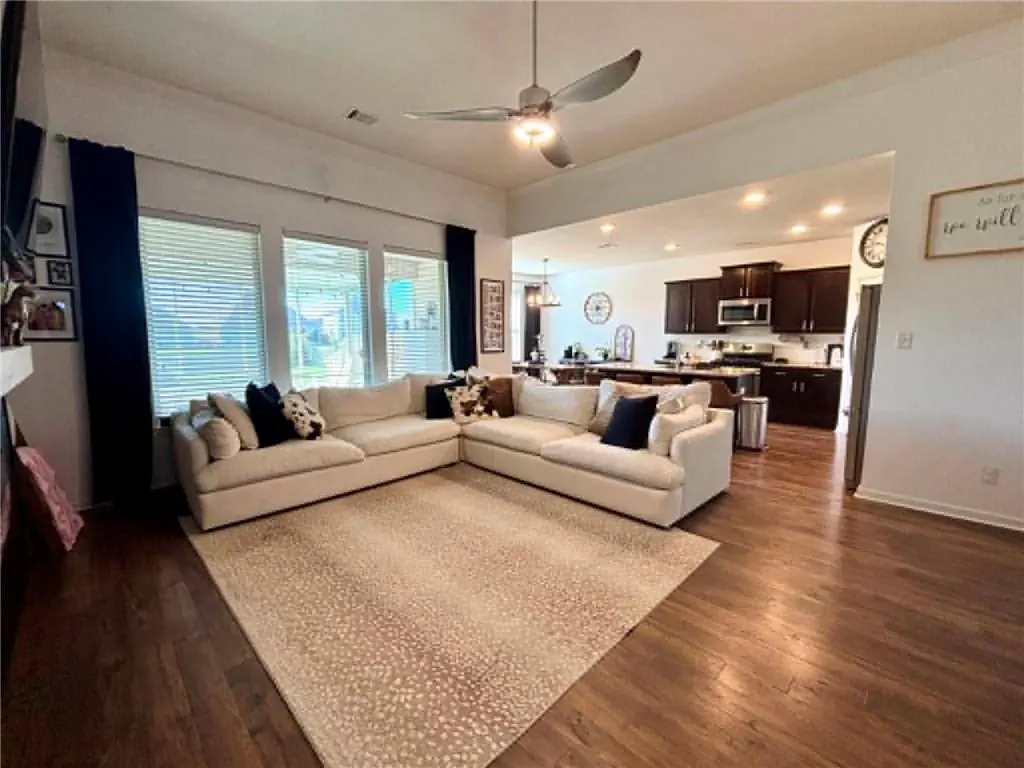 A bright, open-concept living room with a large, cream-colored sectional sofa, a patterned rug, and a view into the kitchen.