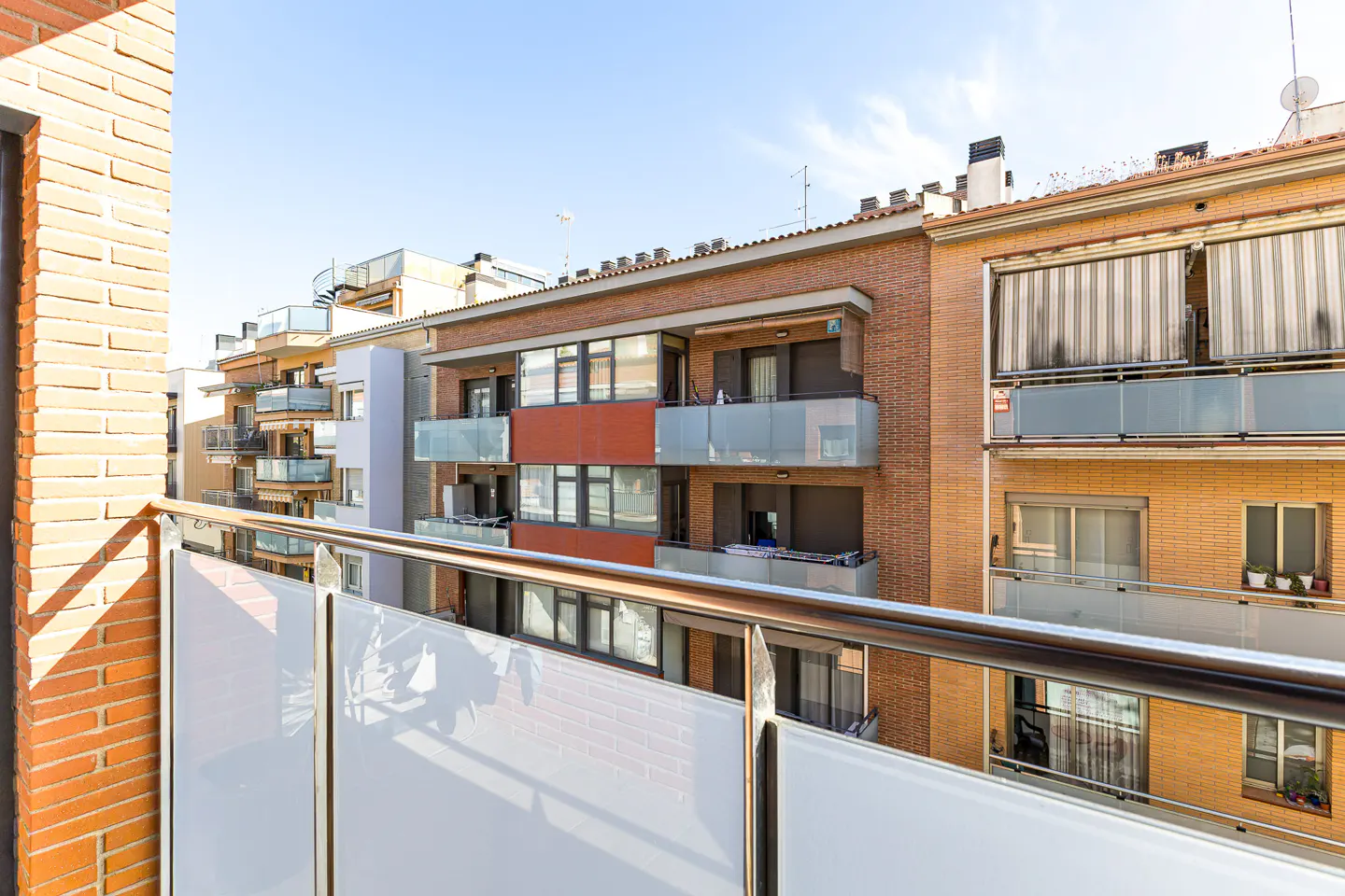 View from a balcony with a metal railing, overlooking brick apartment buildings under a blue sky.