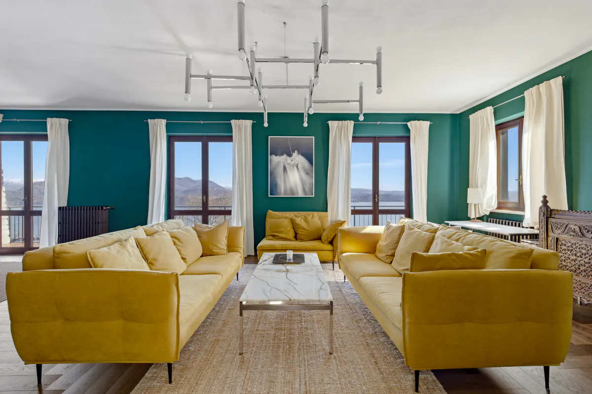 Living room with teal walls, two yellow sofas, a marble coffee table, and a modern chandelier overlooking a lake view.