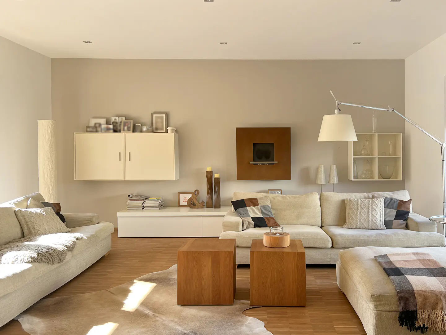 Living room with hardwood floors, two sofas, and two wooden cube tables on a cowhide rug. Cream walls and modern decor.