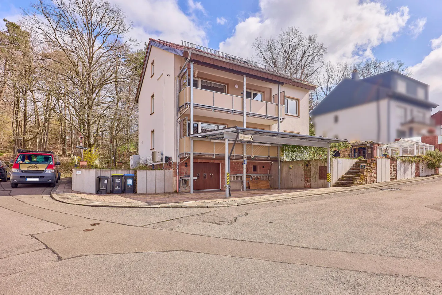 A three-story beige house with a balcony and a carport on a sunny day.