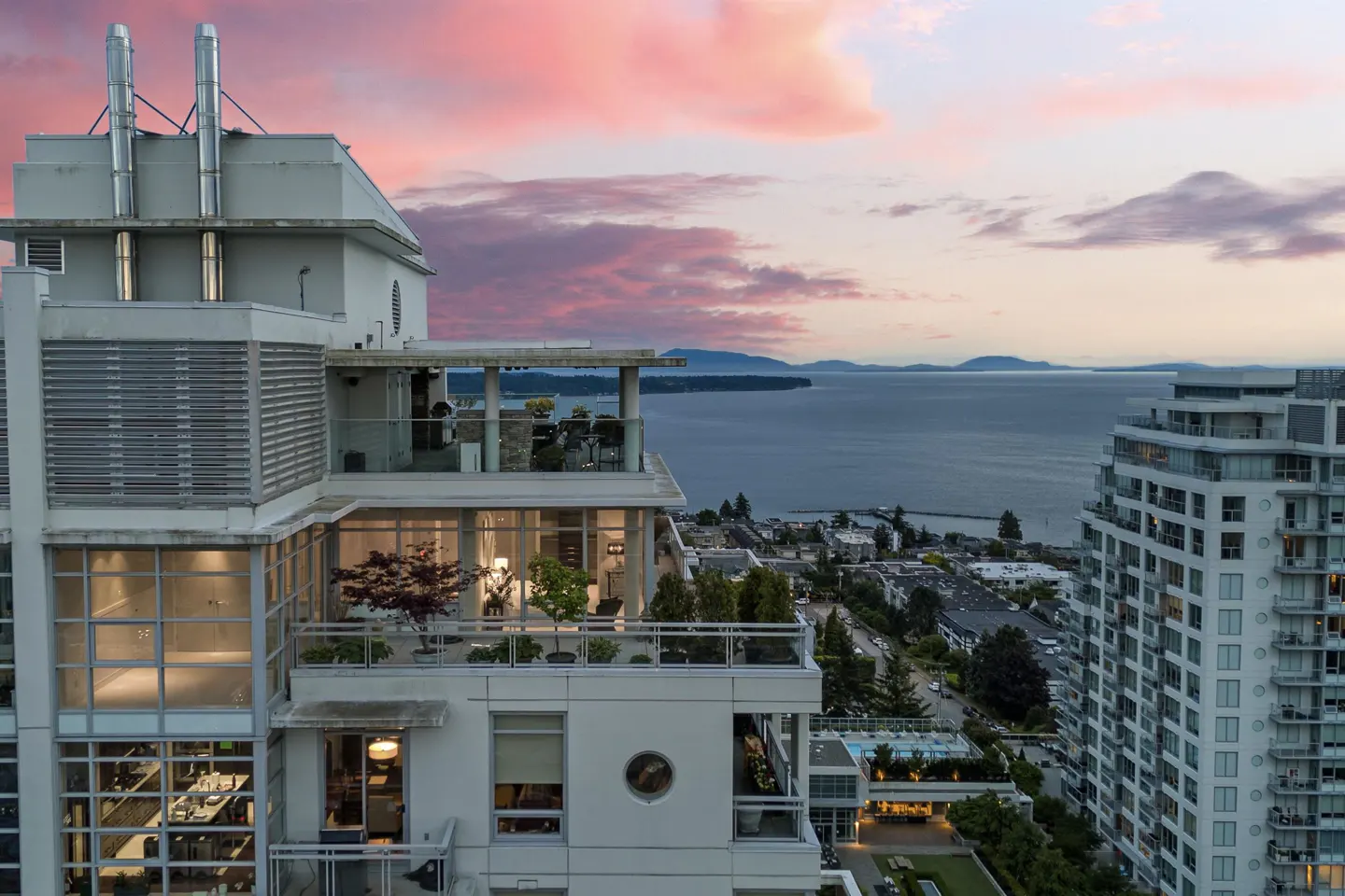 Exterior view of a modern white high-rise condo building with balconies overlooking the ocean at sunset.