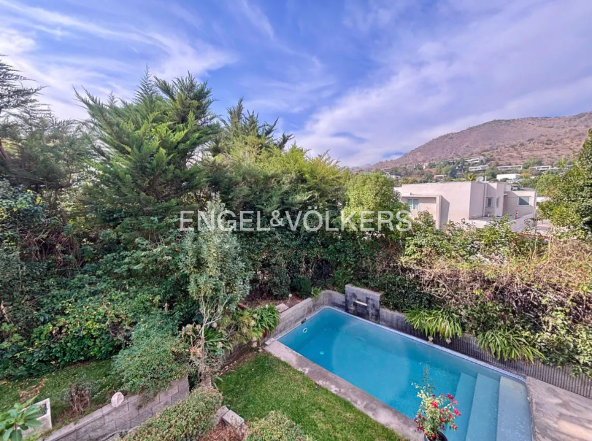 Aerial view of a backyard with a blue swimming pool, green trees, and a mountain in the background.