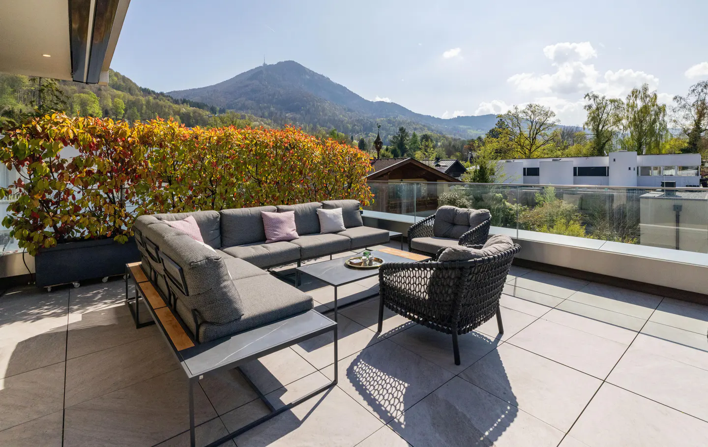 Outdoor patio with gray furniture, including a sectional sofa and chairs, on a tiled floor with a mountain view.