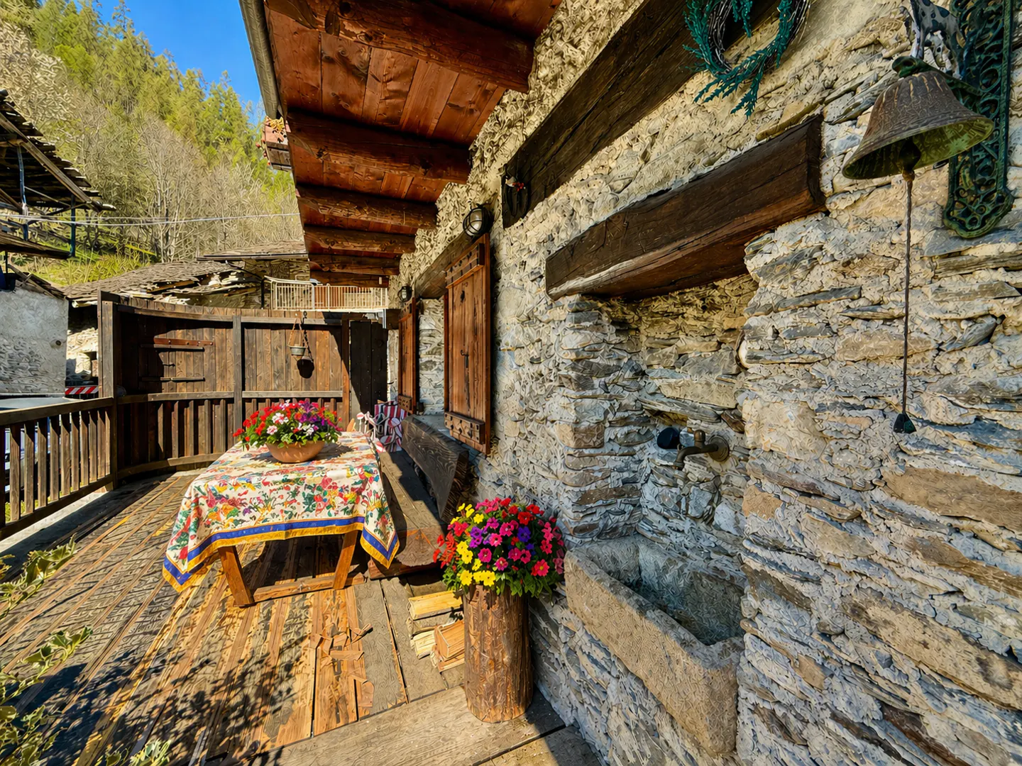 Stone house exterior with wood beams, a table with a floral tablecloth, and colorful flowers in a log planter.