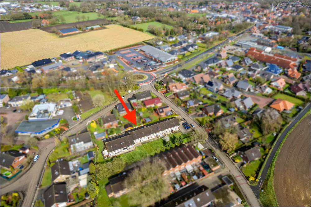 Aerial view of a row of townhouses with a red arrow pointing to one, surrounded by green lawns and other houses.
