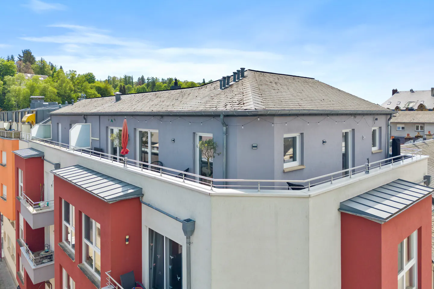 Exterior view of a modern apartment building with a rooftop terrace and colorful facade under a blue sky.