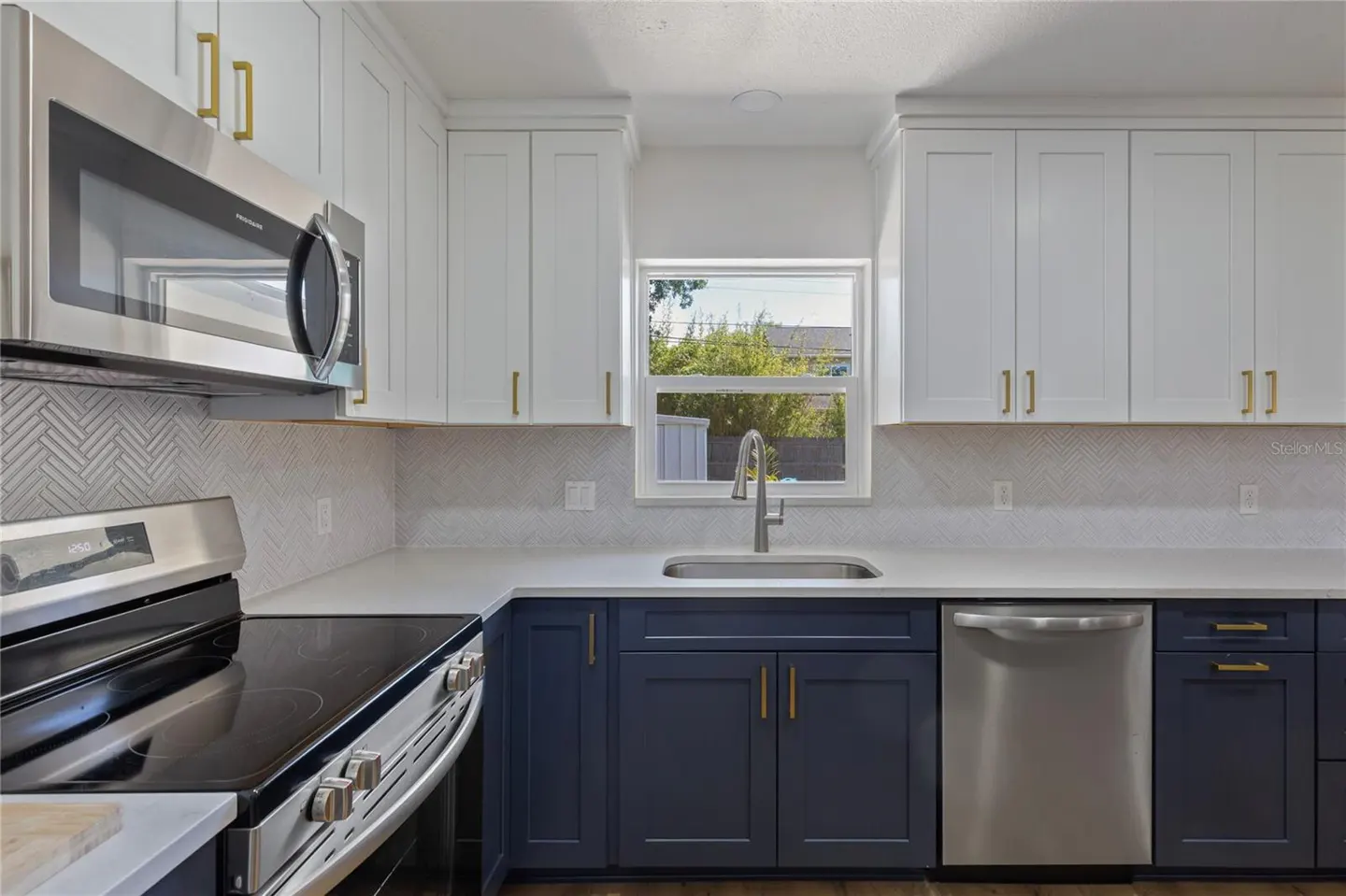 A modern kitchen with white upper cabinets, navy blue lower cabinets, gold hardware, and stainless steel appliances.