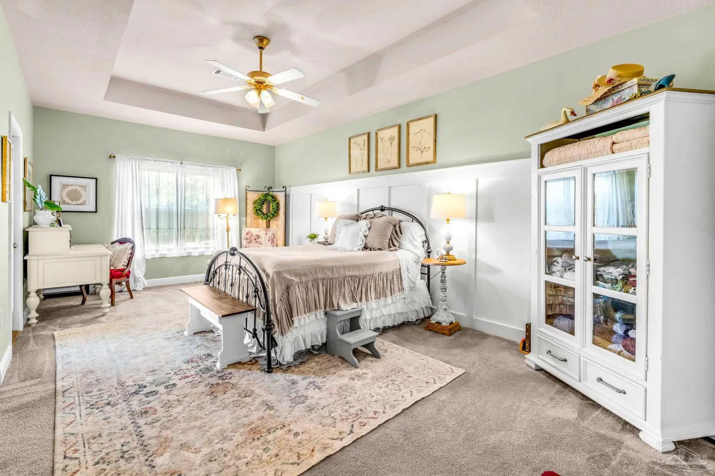A bedroom with light green walls, a black metal bed frame, and a white armoire. A ceiling fan hangs above.