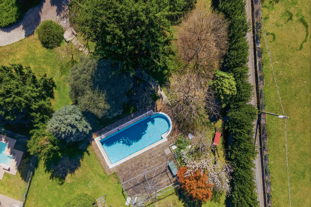 Aerial view of a rectangular swimming pool with blue water, surrounded by green grass and trees.