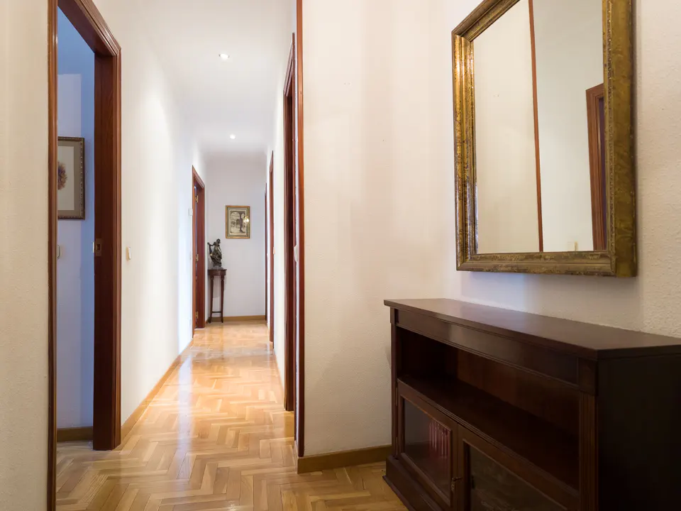 Hallway with wood floors, white walls, and dark wood trim. A gold-framed mirror hangs above a dark wood cabinet.