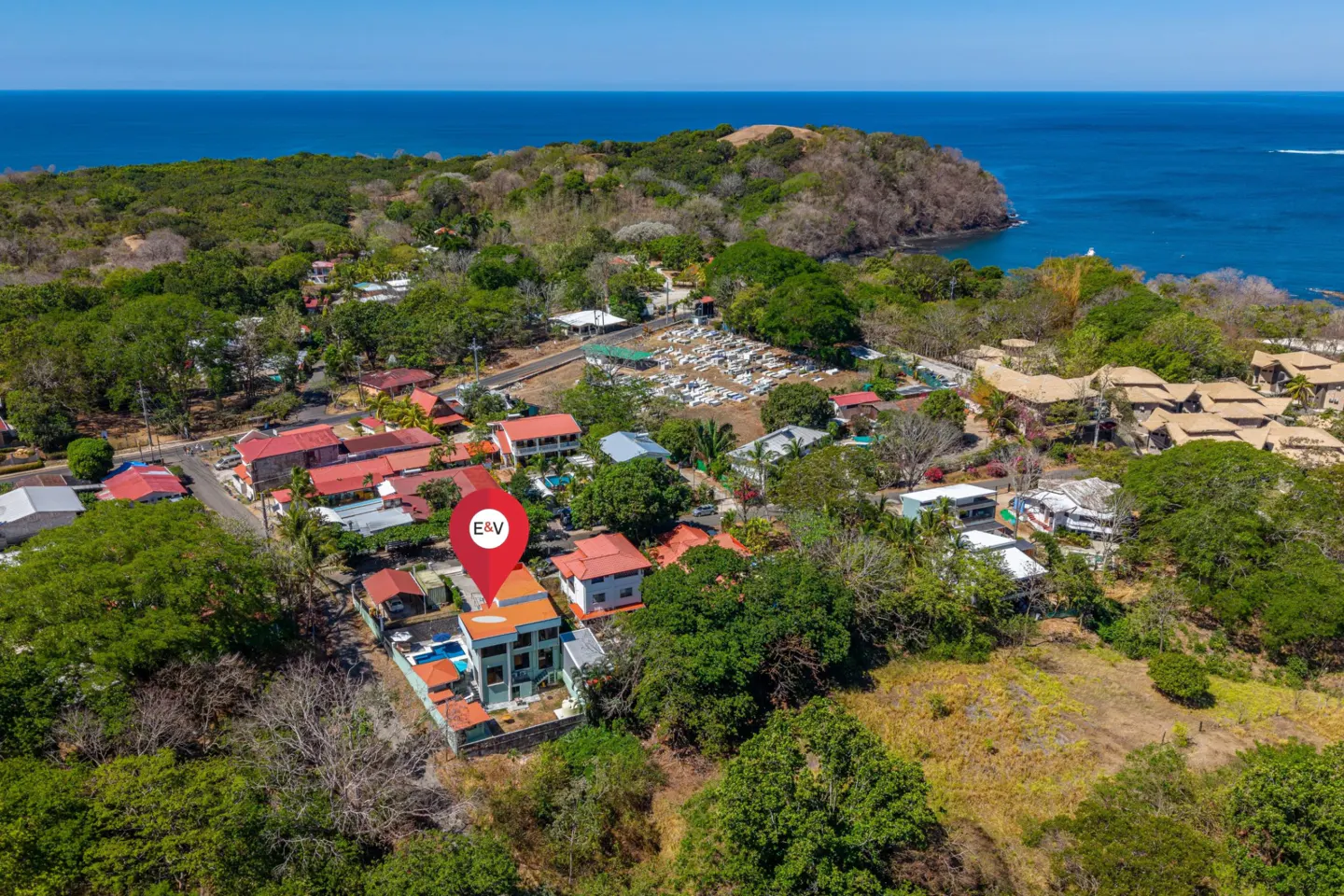 Aerial view of a property with a red pin marker, surrounded by lush greenery and the ocean in the background.