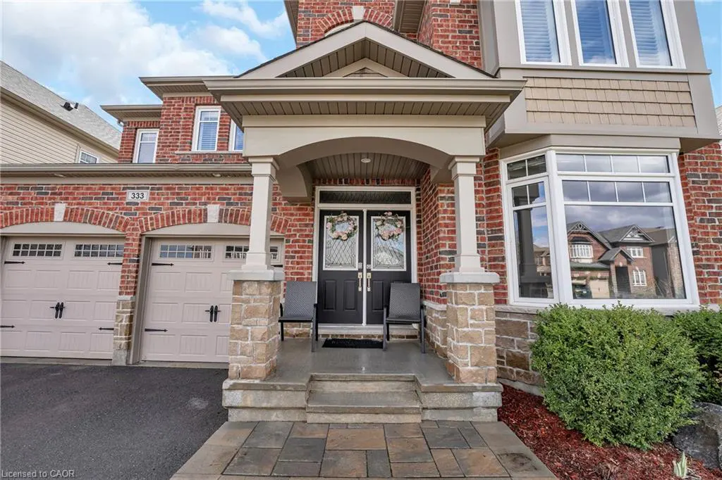 Exterior of a two-story brick house with a double garage and a covered front porch with two black chairs.