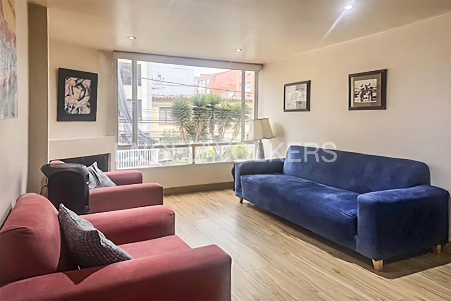 Living room with a blue sofa, two red armchairs, and a large window with a view of buildings and trees.