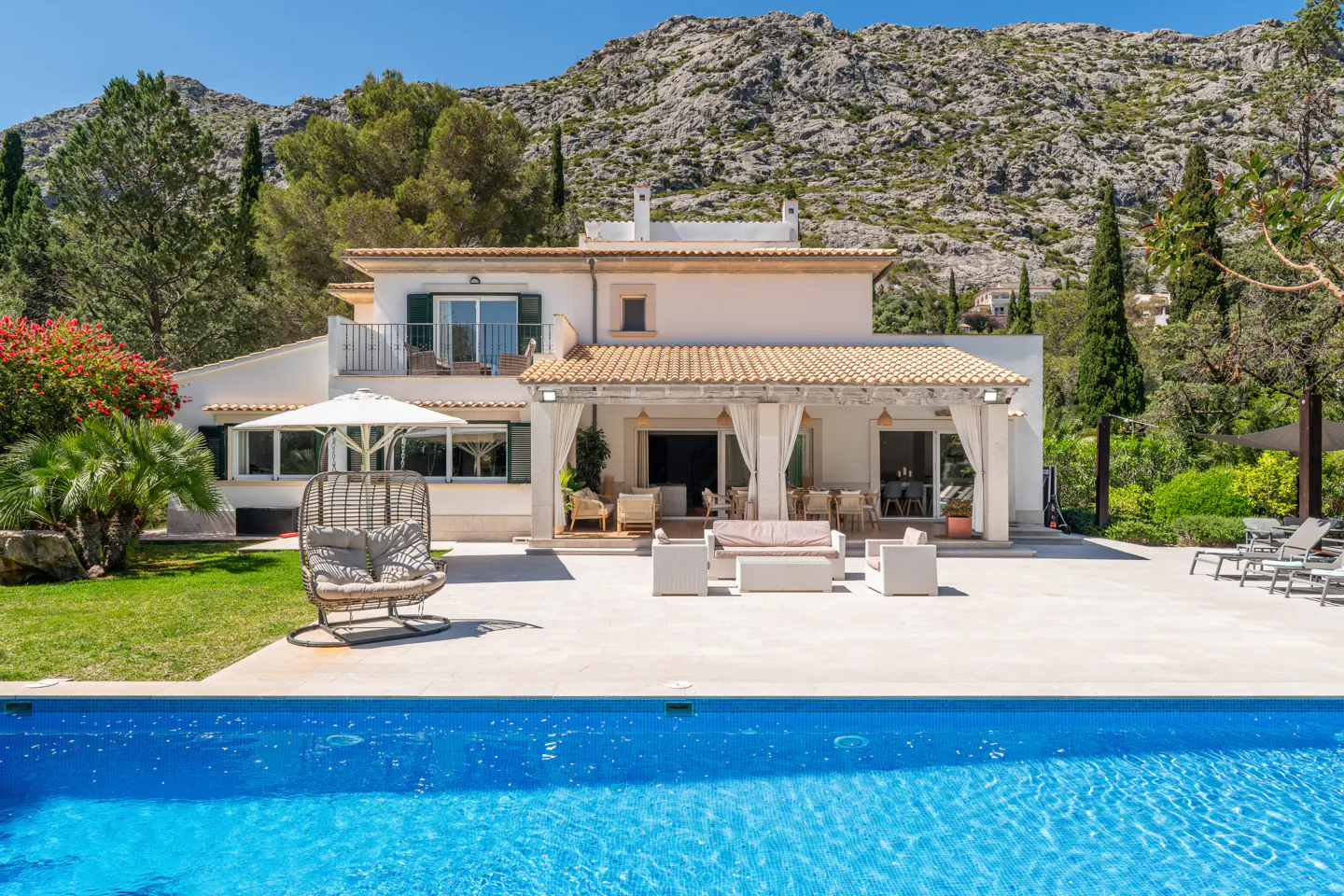 A two-story white house with a pool, patio furniture, and mountain backdrop.