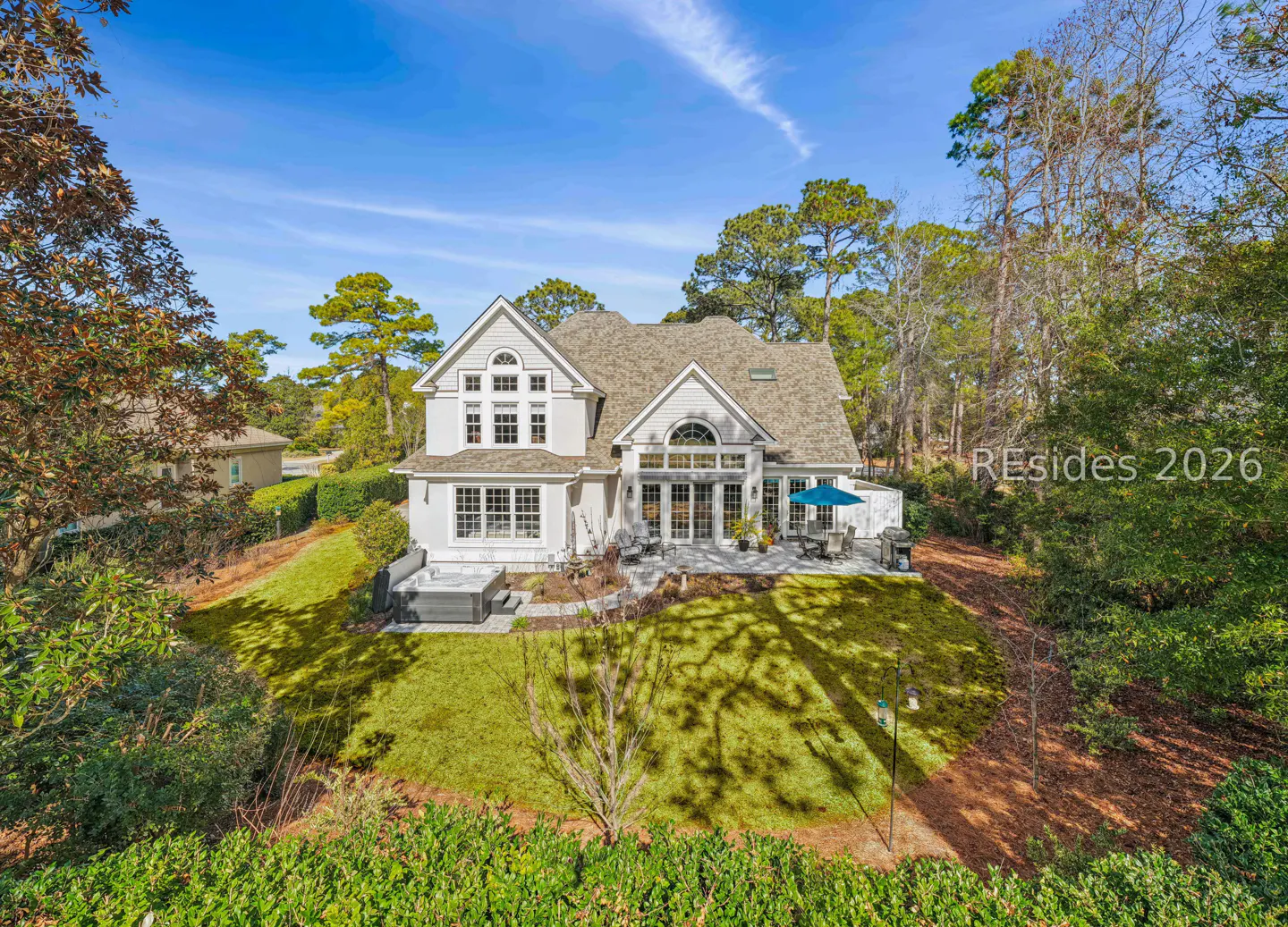 Two-story light gray house with a brown roof, a patio, and a green lawn on a sunny day.