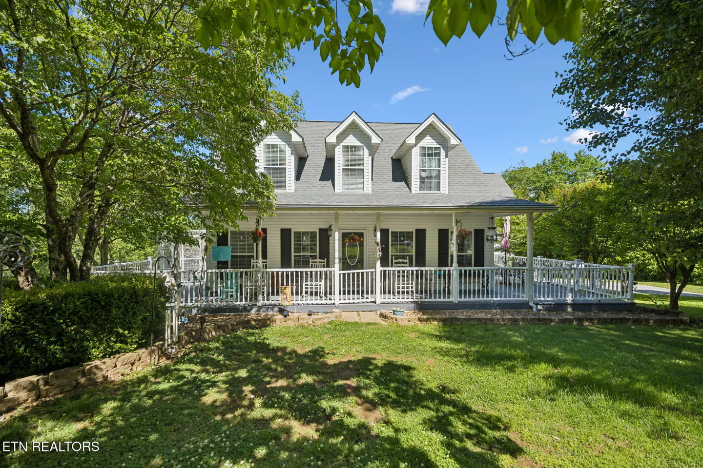 Exterior of a white, two-story house with a gray roof and black shutters, surrounded by green trees and lawn.