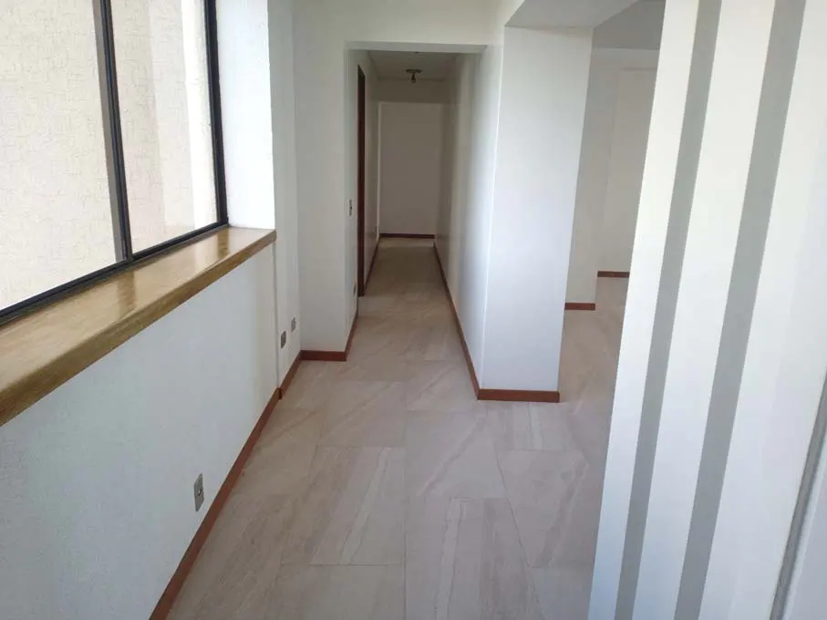A bright hallway with white walls, light tile floors, and a wooden window ledge. A doorway leads to another room.